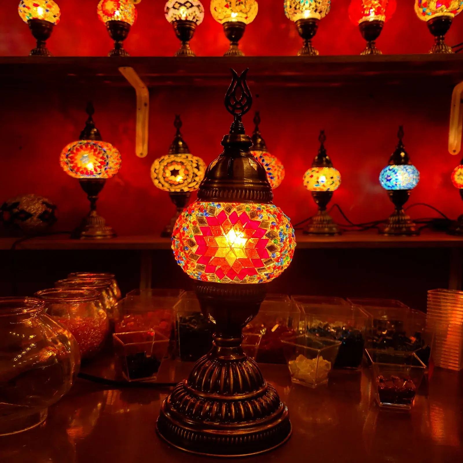 A red star-pattern mosaic lamp on the workbench, shelves of glowing lamps behind in our Balat workshop