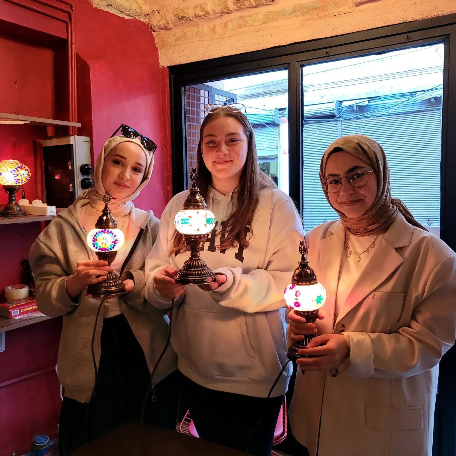 Hands placing mosaic tiles onto a lamp globe at our Balat workshop, surrounded by glass-tile sorting trays