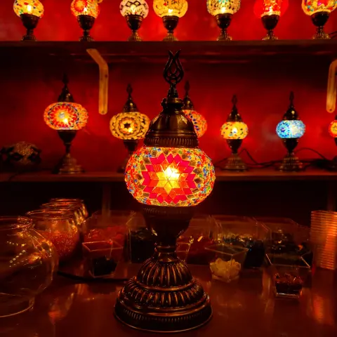 A lit lamp on the worktable, with shelves of glowing lamps behind it